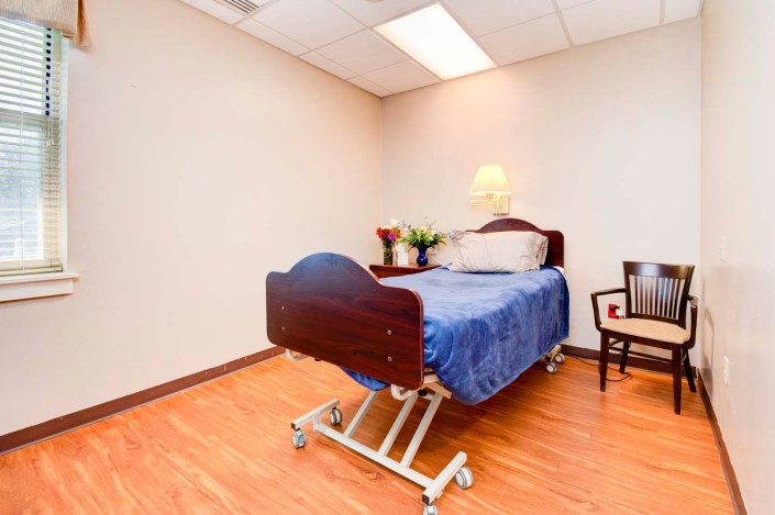 A hospital room with a single bed and a chair, featuring simple decor.