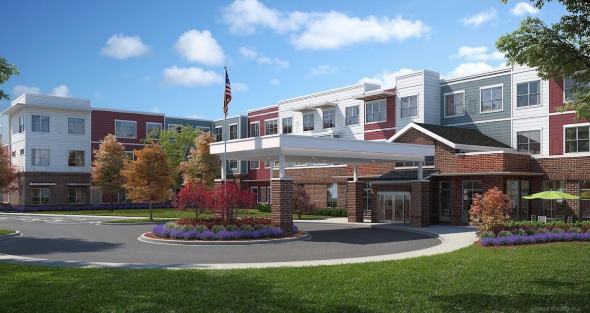 A modern hospital building with a landscaped entrance and an American flag flying under a blue sky.
