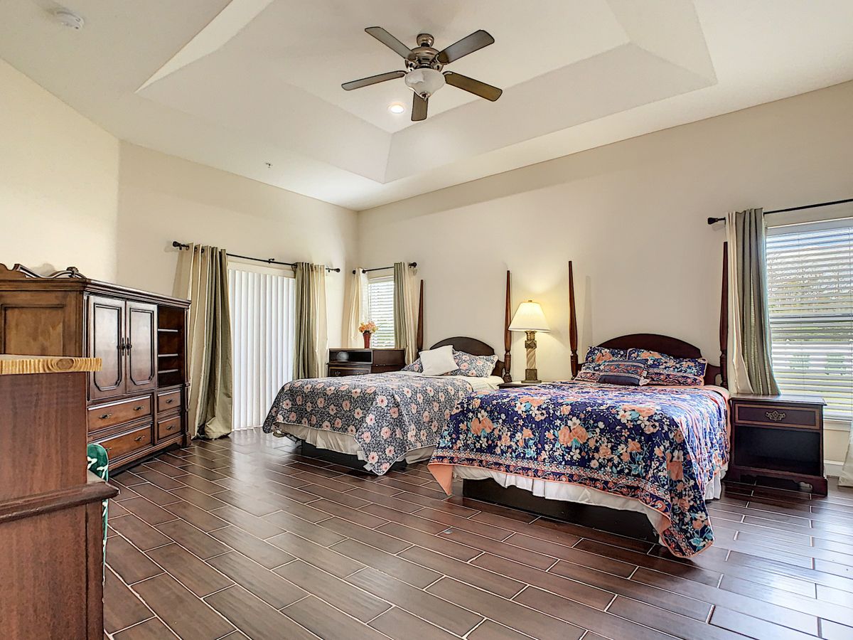 A spacious bedroom with two beds, wooden flooring, and a ceiling fan.