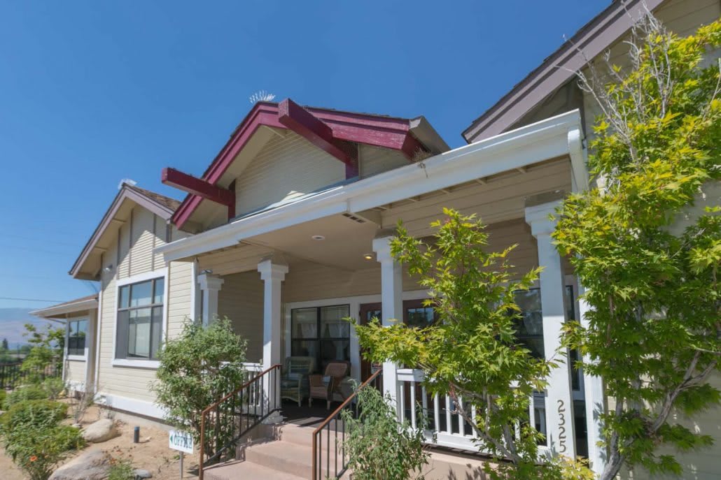 A residential house with a front porch and surrounding greenery under a clear blue sky.