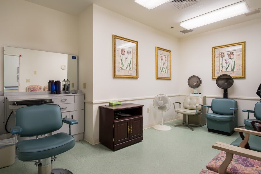 A cozy salon room featuring styling chairs, a mirror, hair dryer, and floral artwork on the walls.
