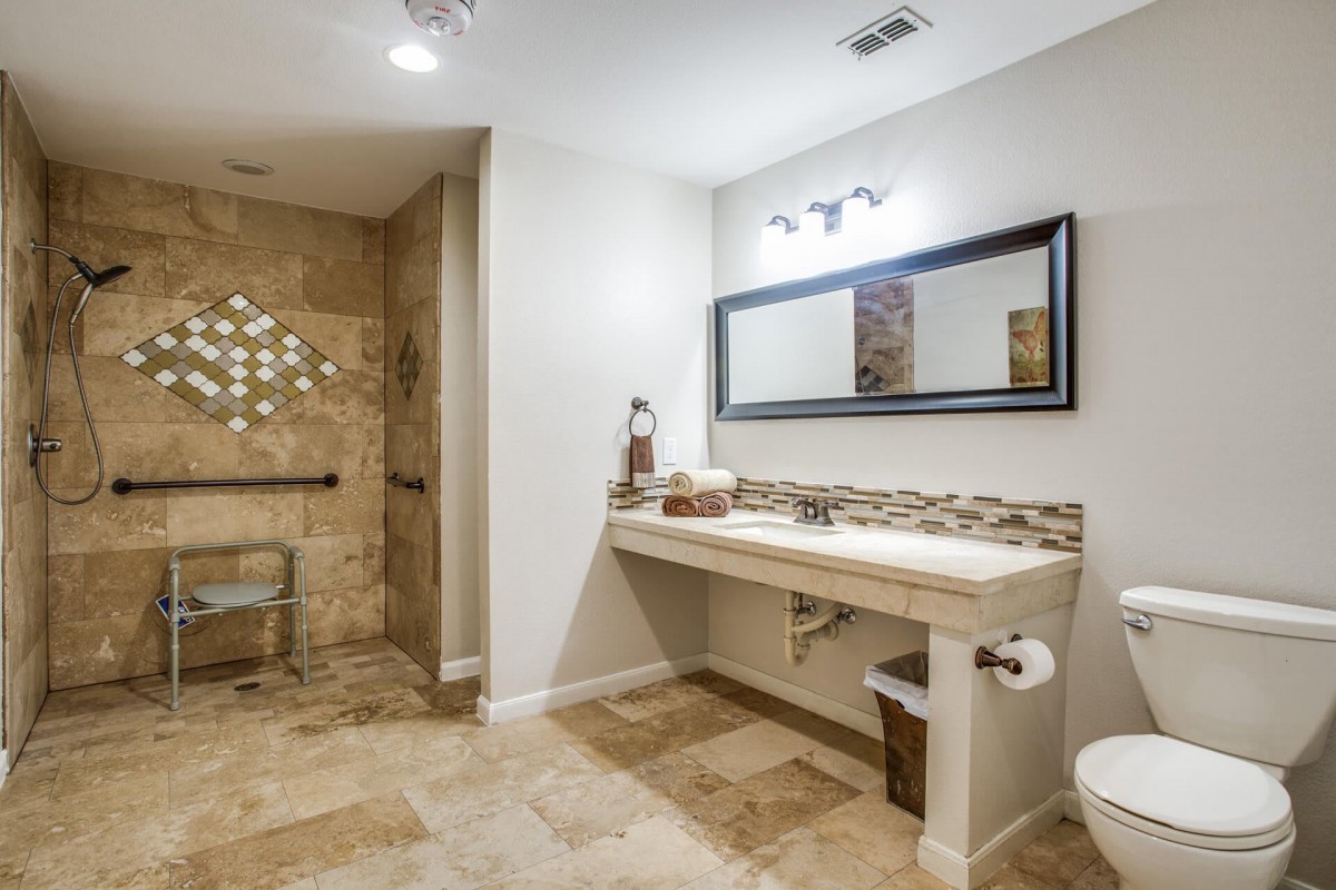 A modern and accessible bathroom with a large mirror, sink, and tiled shower area.