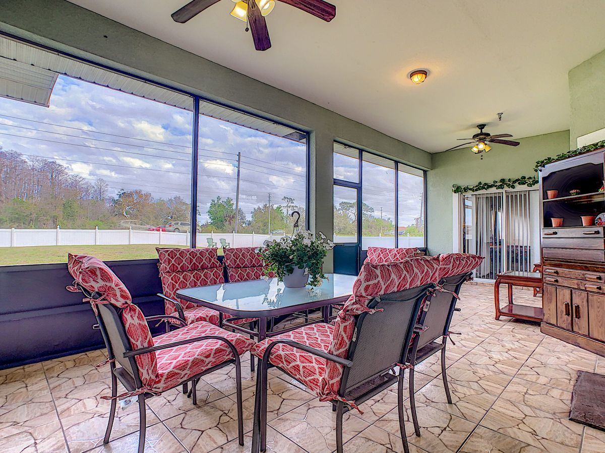 A cozy sunroom with a dining table and chairs, surrounded by large glass windows and decorated with indoor plants.