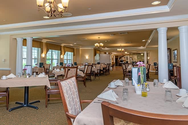 An elegantly set dining area with multiple tables and chairs, featuring chandeliers and a warm ambiance.