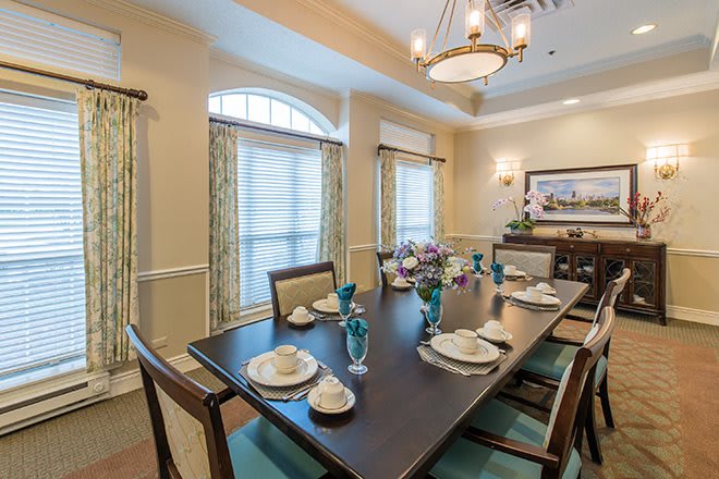 A well-decorated dining room with a long table set for a meal, featuring elegant dinnerware and a chandelier overhead.