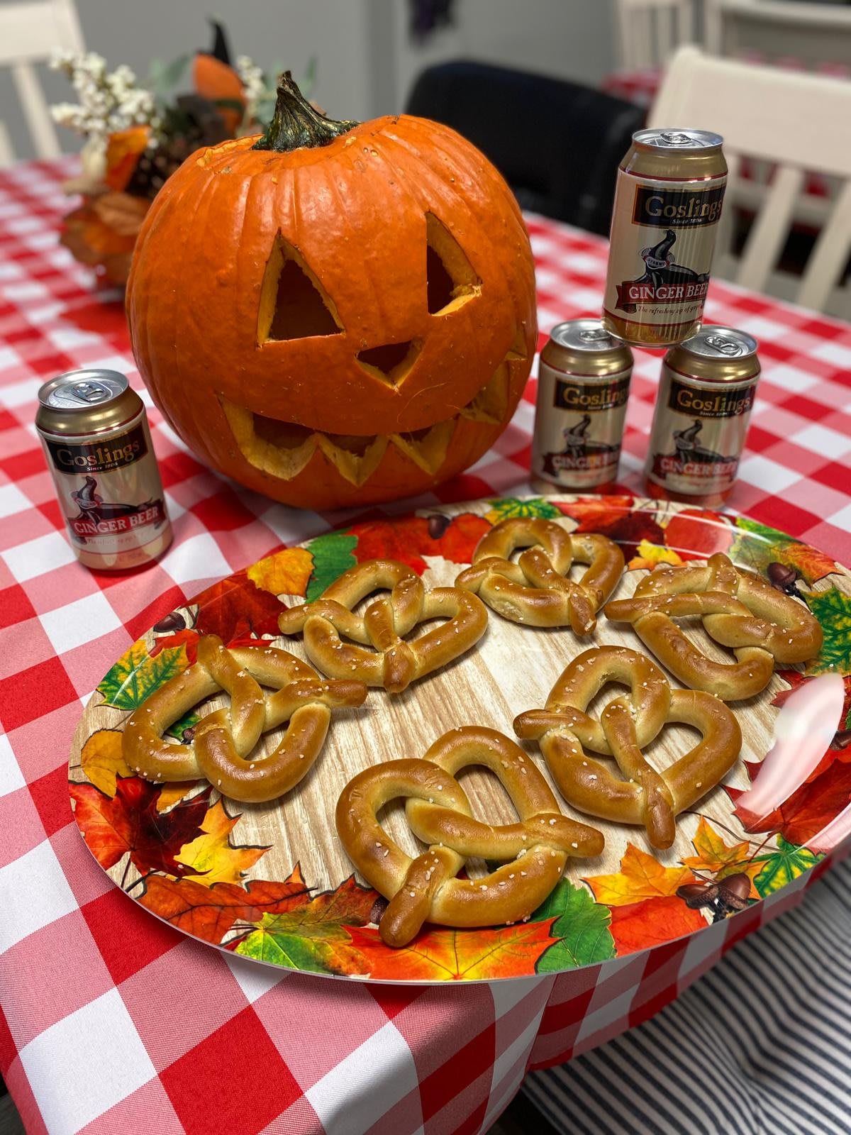 A festive Halloween setup with a carved pumpkin and pretzels on a colorful plate, accompanied by beers.