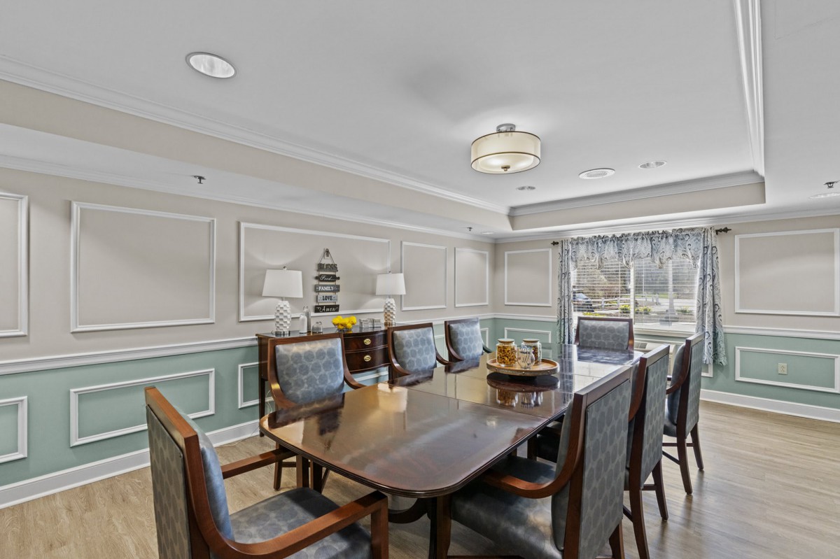 An elegantly decorated dining room with a wooden table and upholstered chairs, featuring a chandelier and refined wall decor.
