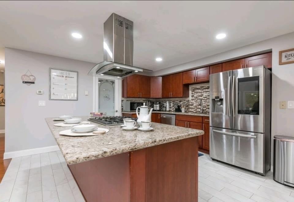 A modern kitchen featuring a large island with granite countertops, surrounded by wood cabinets and stainless steel appliances.