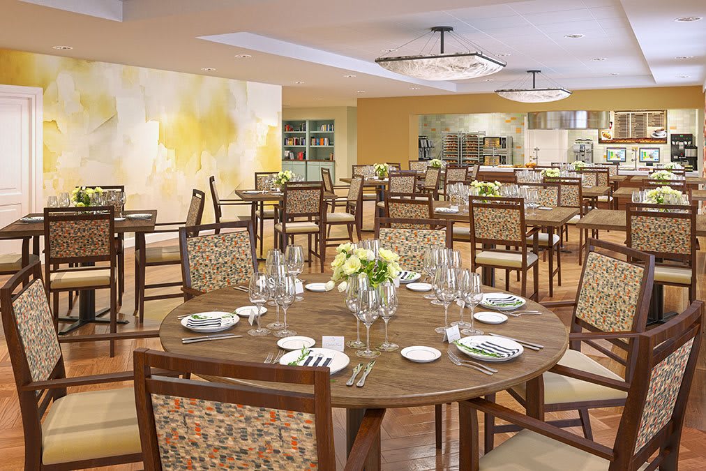A beautifully set dining room with round wooden tables, decorated with flowers and neatly arranged place settings.