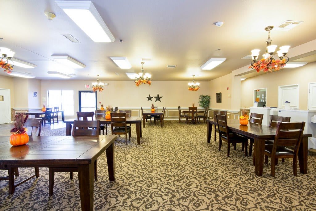 A spacious and well-lit dining room with multiple tables and chairs arranged on a patterned carpet.
