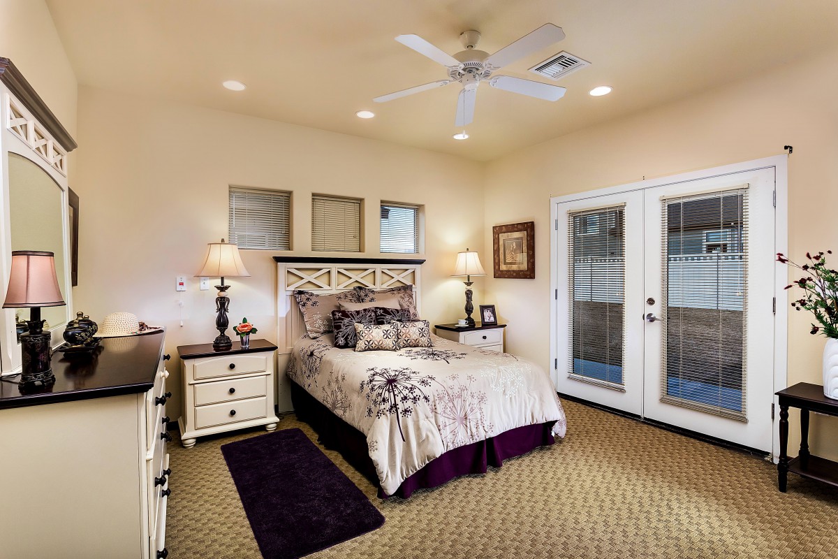 A cozy bedroom with elegant decor, featuring a neatly made bed, bedside lamps, and French doors leading outside.