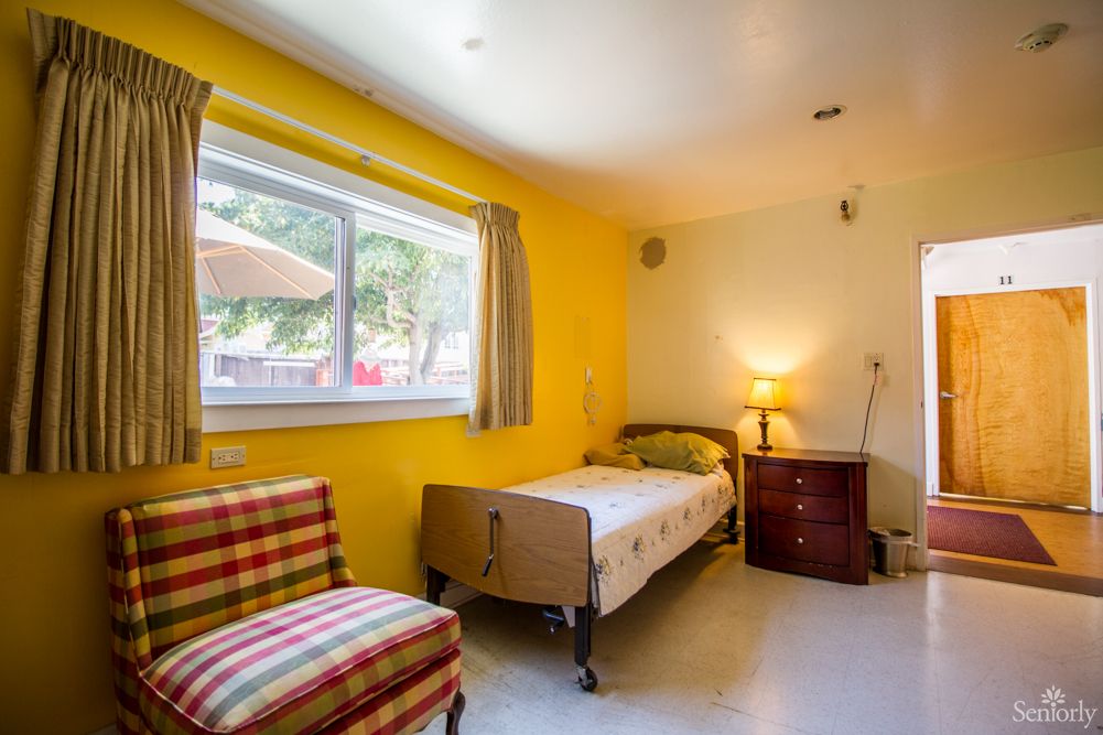 A cozy bedroom with yellow walls, featuring a single bed and a bright window.
