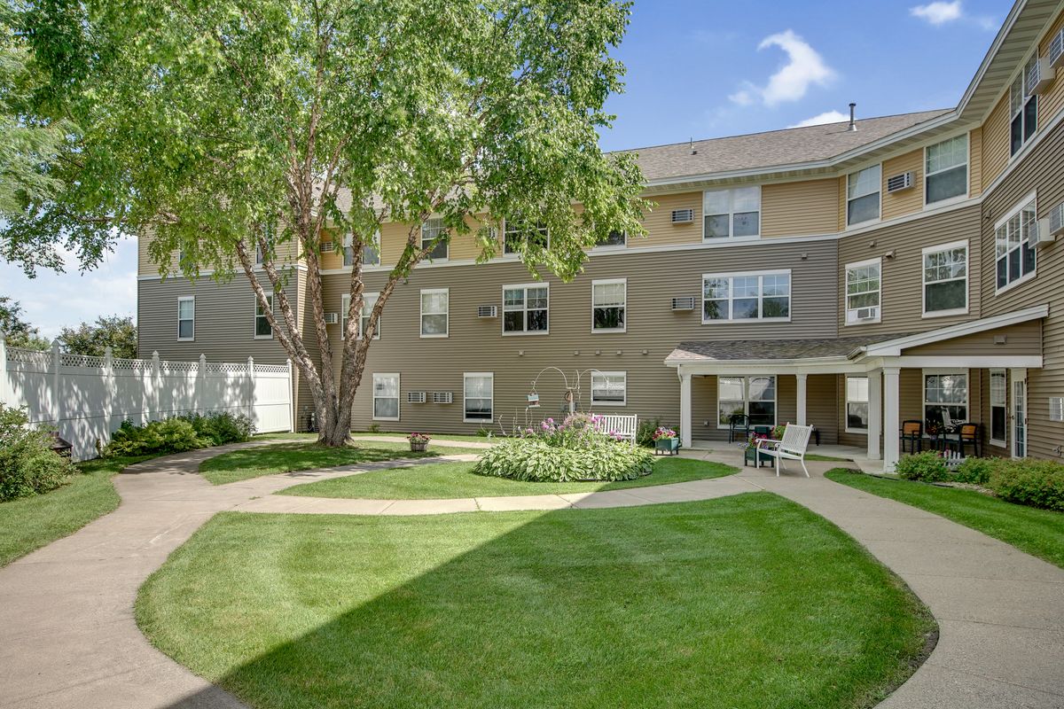 A residential apartment building with a courtyard featuring a well-maintained lawn, trees, and outdoor seating area.