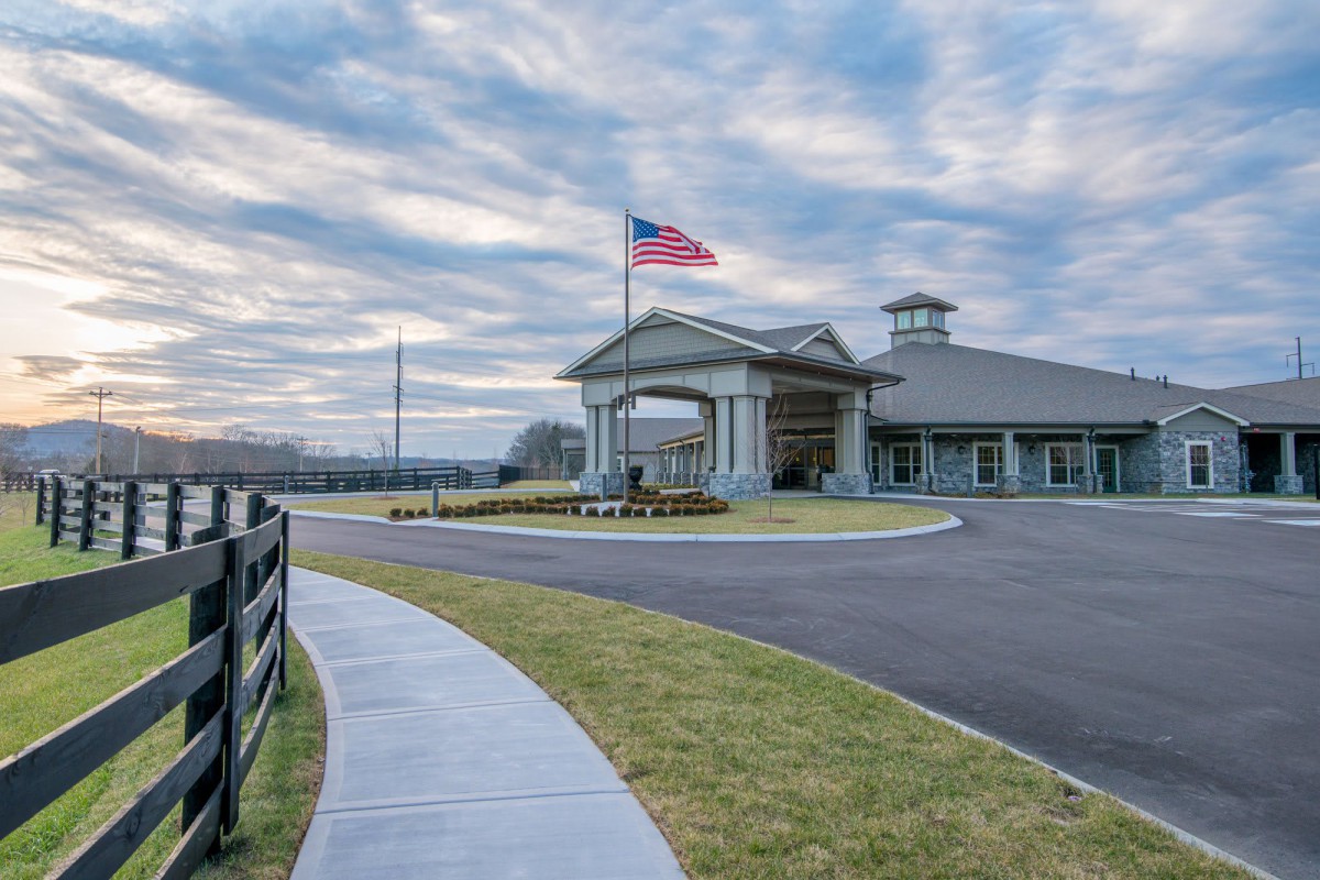 A building with an American flag flying, surrounded by a paved walkway and lawn under a cloudy sky.