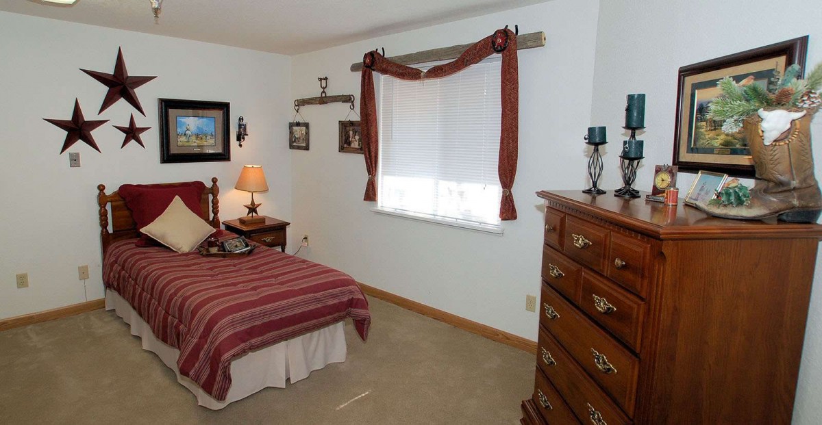 A cozy bedroom with a single bed, dresser, and window adorned with red curtains.