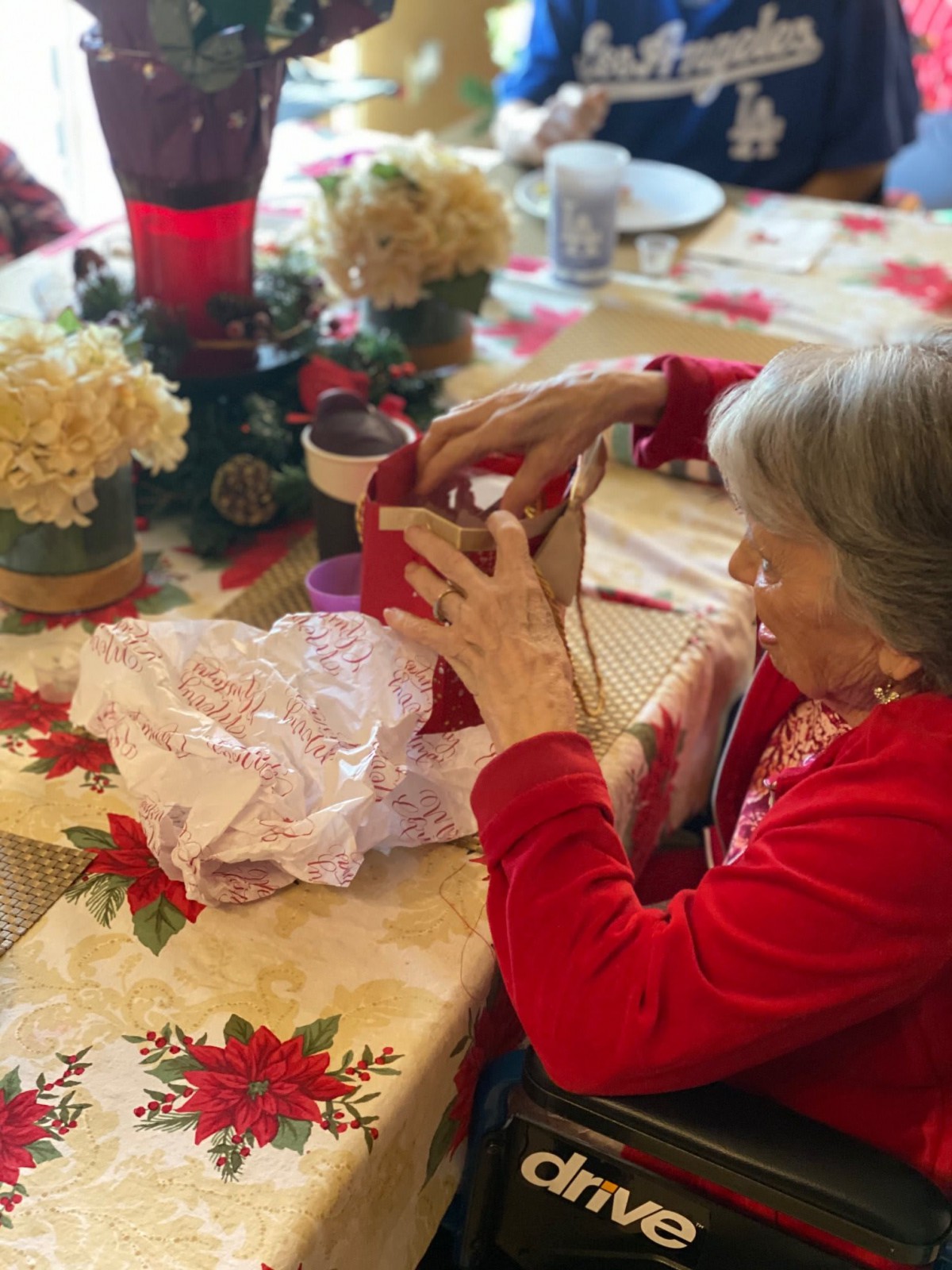An elderly woman joyfully wraps a gift at a festive Christmas table.