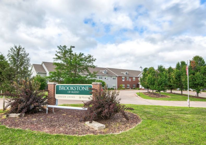 Entrance of a residential apartment complex with landscaped surroundings and clear skies.