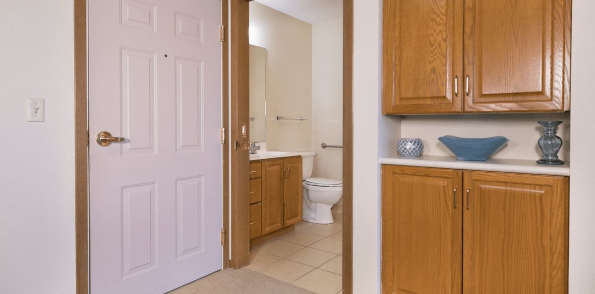 View of a bathroom featuring a toilet, sink with a mirror, and wooden cabinets.