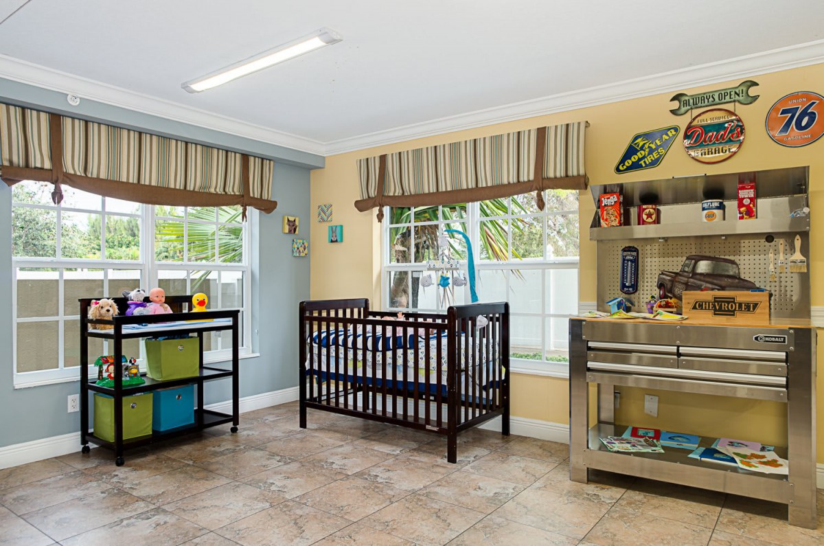 A bright nursery with a crib, shelves filled with toys, and colorful decor by the windows.