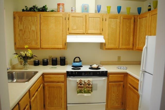 A cozy kitchen with wooden cabinets, a stove, and decorative items on the countertops and shelves.