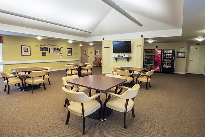 A spacious lounge area with tables and chairs, a television on the wall, and vending machines in the corner.