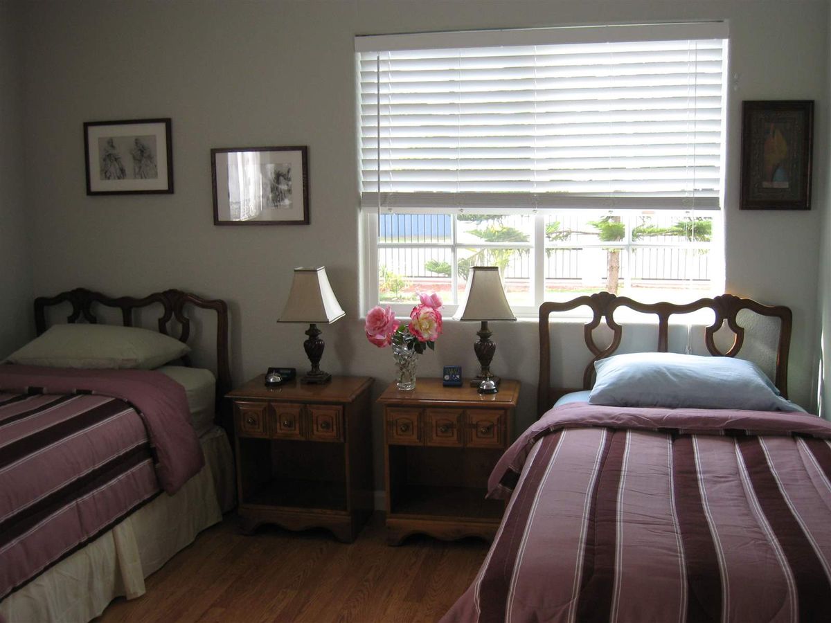 A cozy bedroom with twin beds, nightstands, and lamps by a window with blinds.