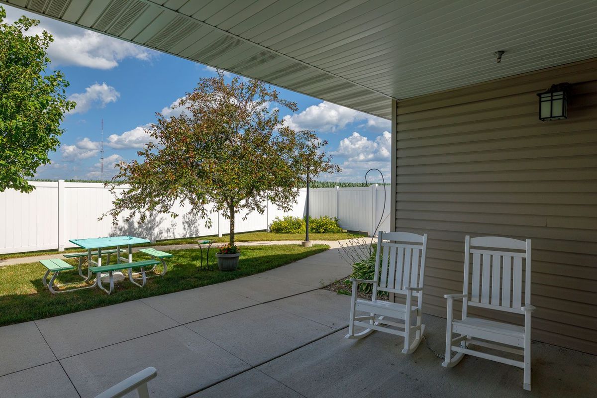 A peaceful backyard patio with rocking chairs overlooking a tree and well-maintained lawn under a blue sky.