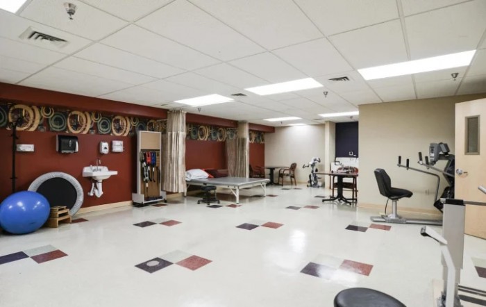 A spacious rehabilitation room equipped with therapy beds, exercise equipment, and privacy curtains.
