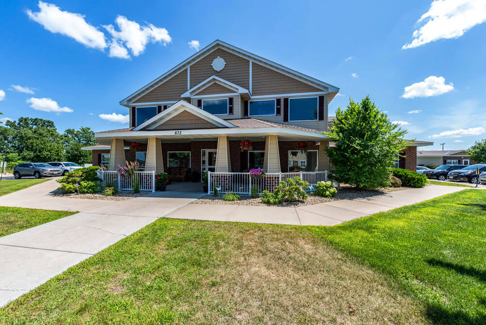 A modern two-story residential house with landscaped front yard under a bright blue sky.