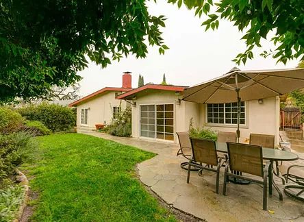 A cozy backyard with a patio, outdoor dining set, and green lawn.