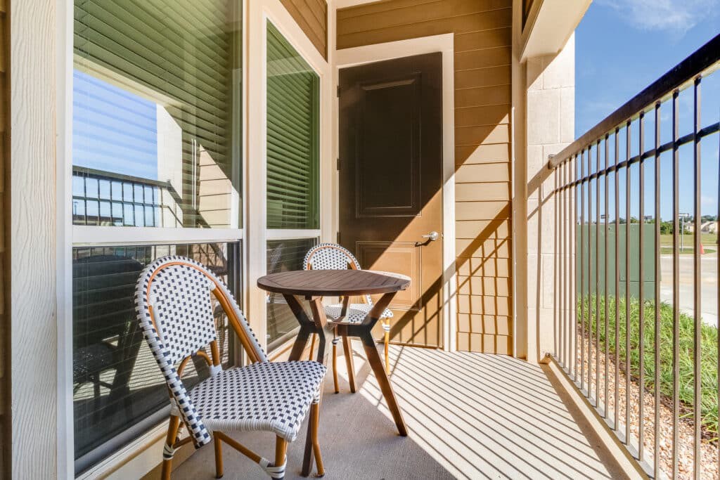 A cozy balcony with two chairs and a small table, bathed in sunlight.