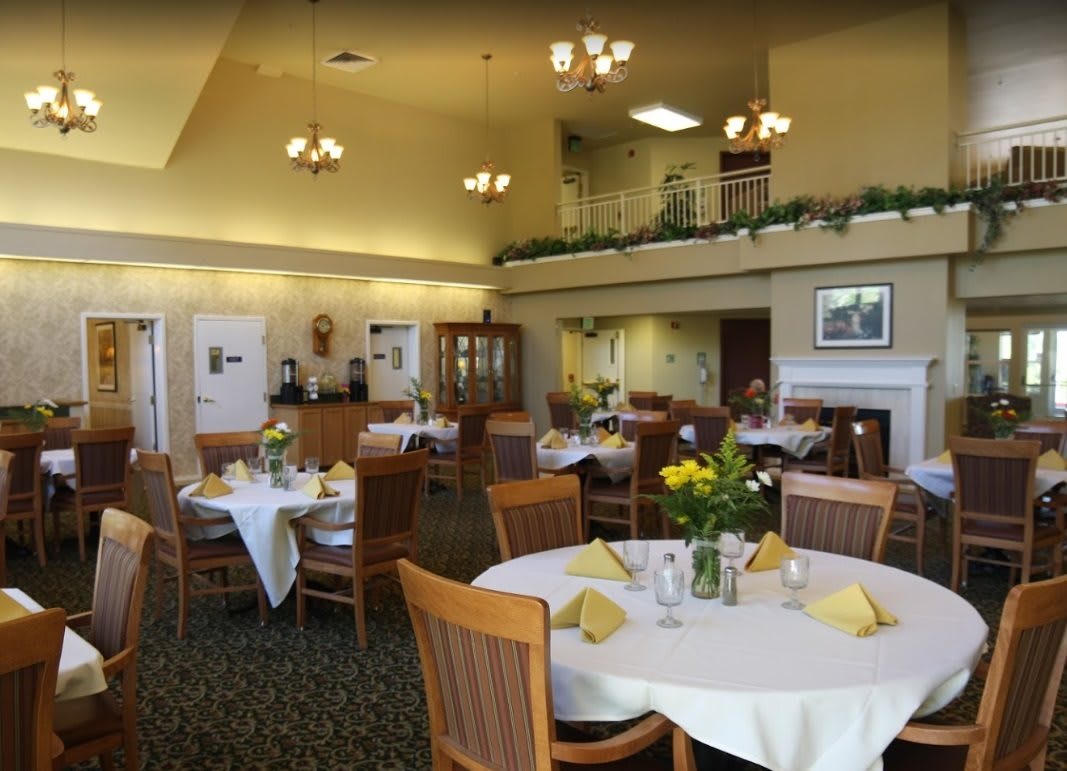An elegant dining room with neatly arranged tables, each set with yellow napkins and floral centerpieces.