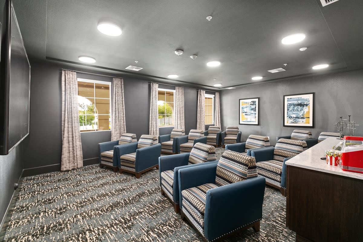 A cozy seating area with multiple chairs, carpeted flooring, and windows adorned with curtains.