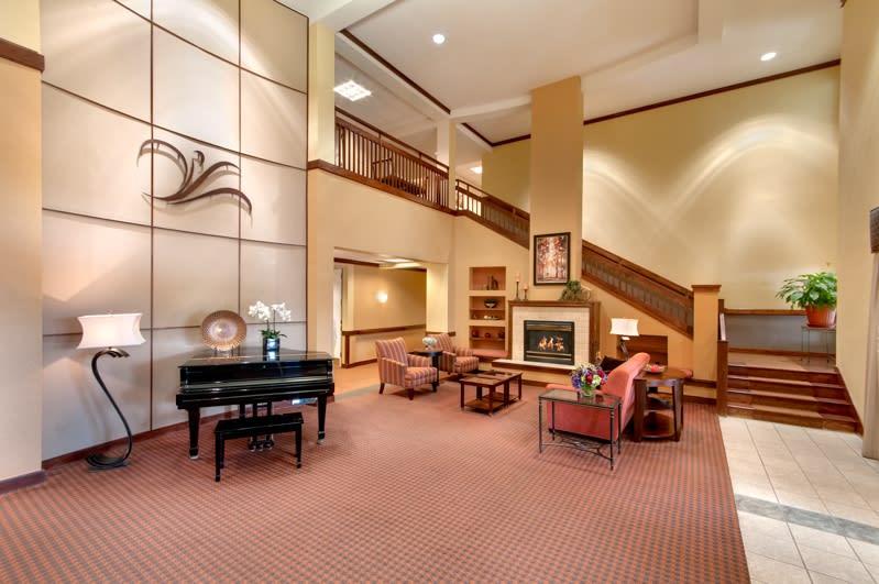 A welcoming lobby with a grand piano, comfortable seating around a fireplace, and an elegant staircase.