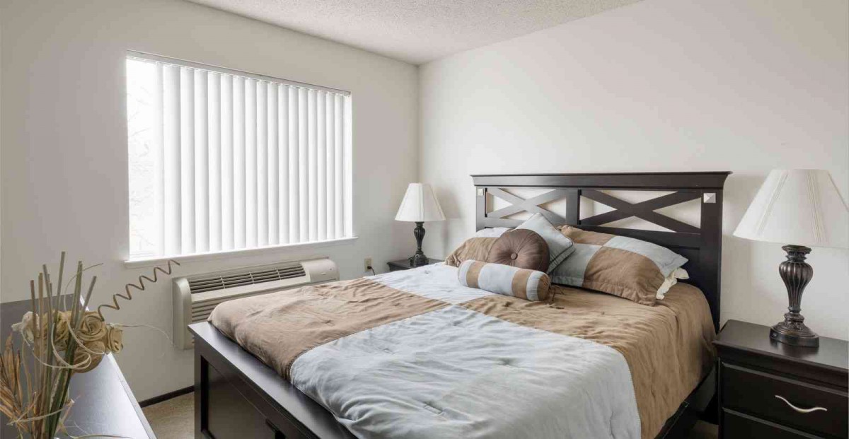 A neatly made bed with pillows next to a window and lamp in a bedroom.