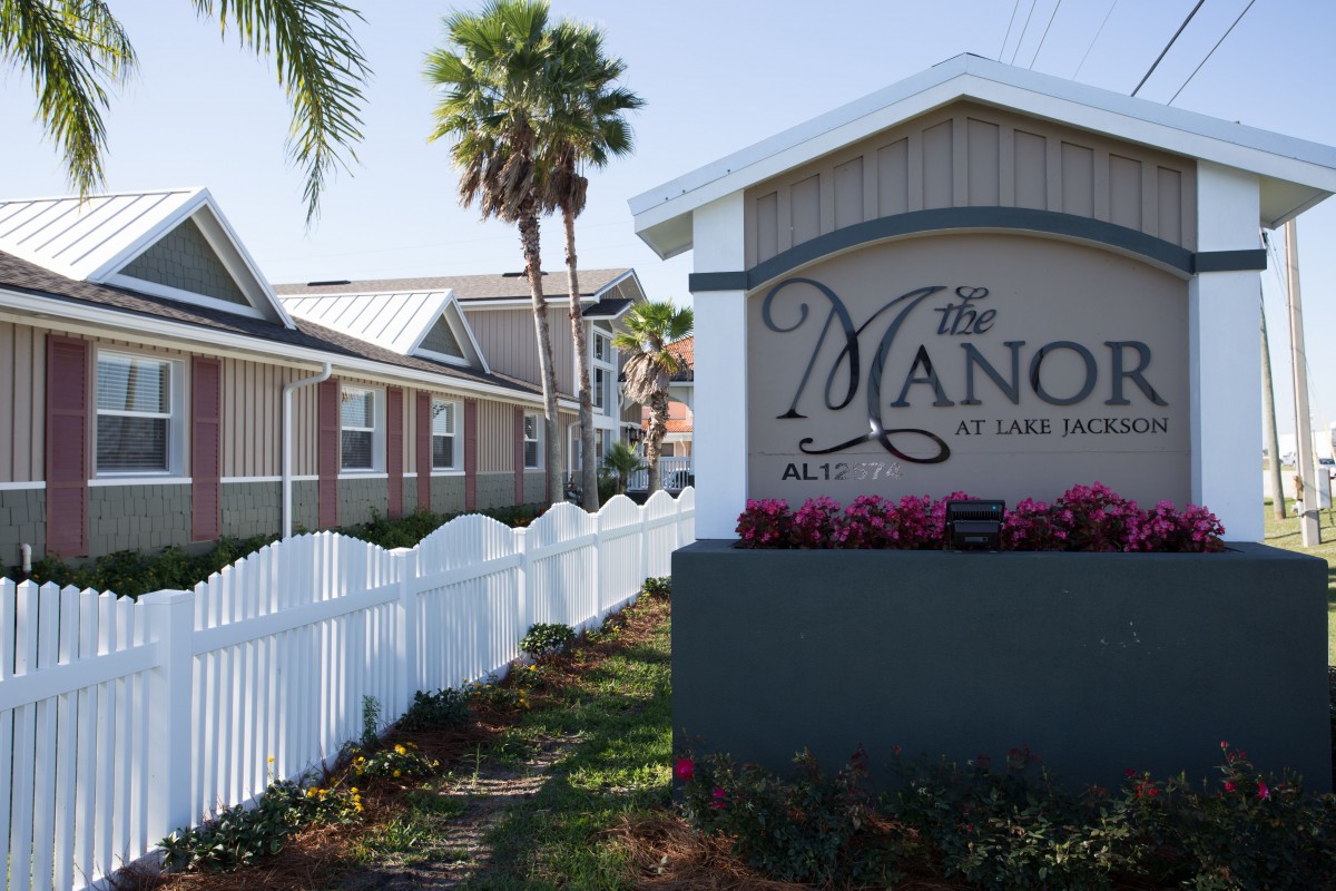 A row of houses with a white picket fence and palm trees, featuring a sign for 'The Manor'.