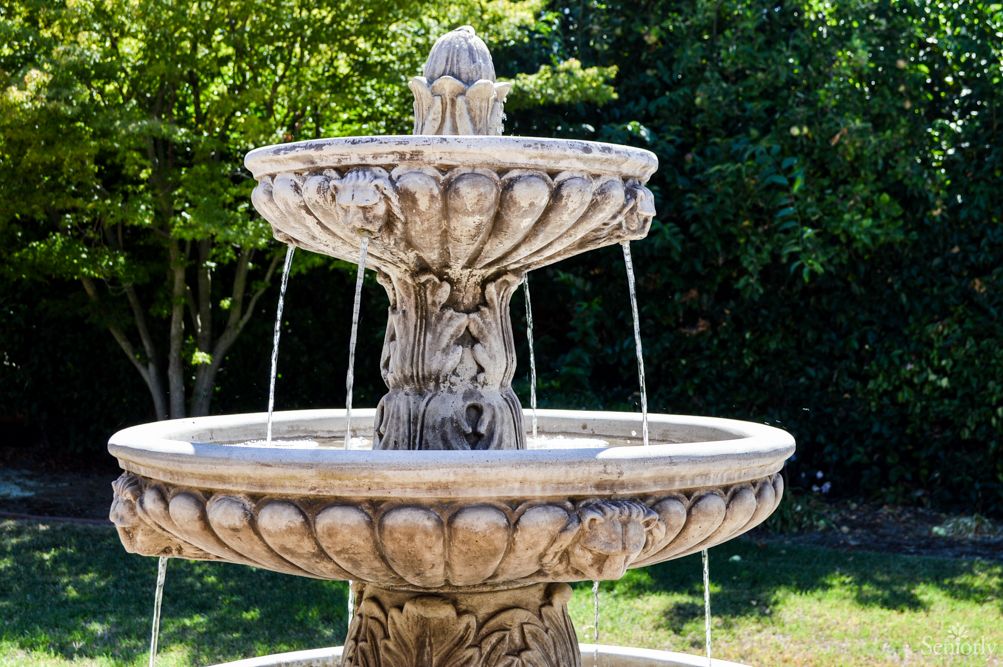 A stone fountain in a garden setting, with water cascading from the top tier.