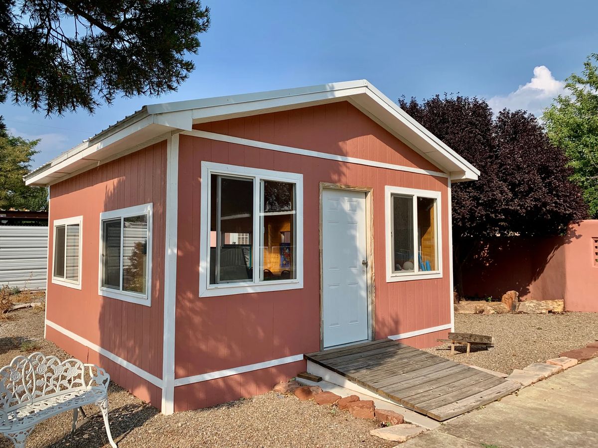 A small red tiny house with a ramp and large windows.