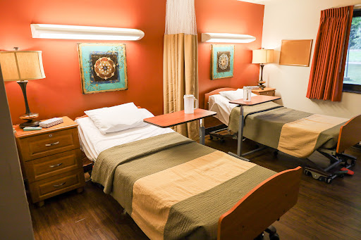 A modern hospital room featuring two beds, equipped with warm lighting and colorful artwork on the walls.