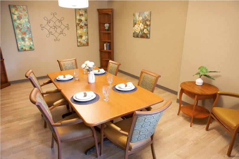 A well-decorated dining room with a wooden table set for a meal, surrounded by upholstered chairs and adorned with wall art and decorations.