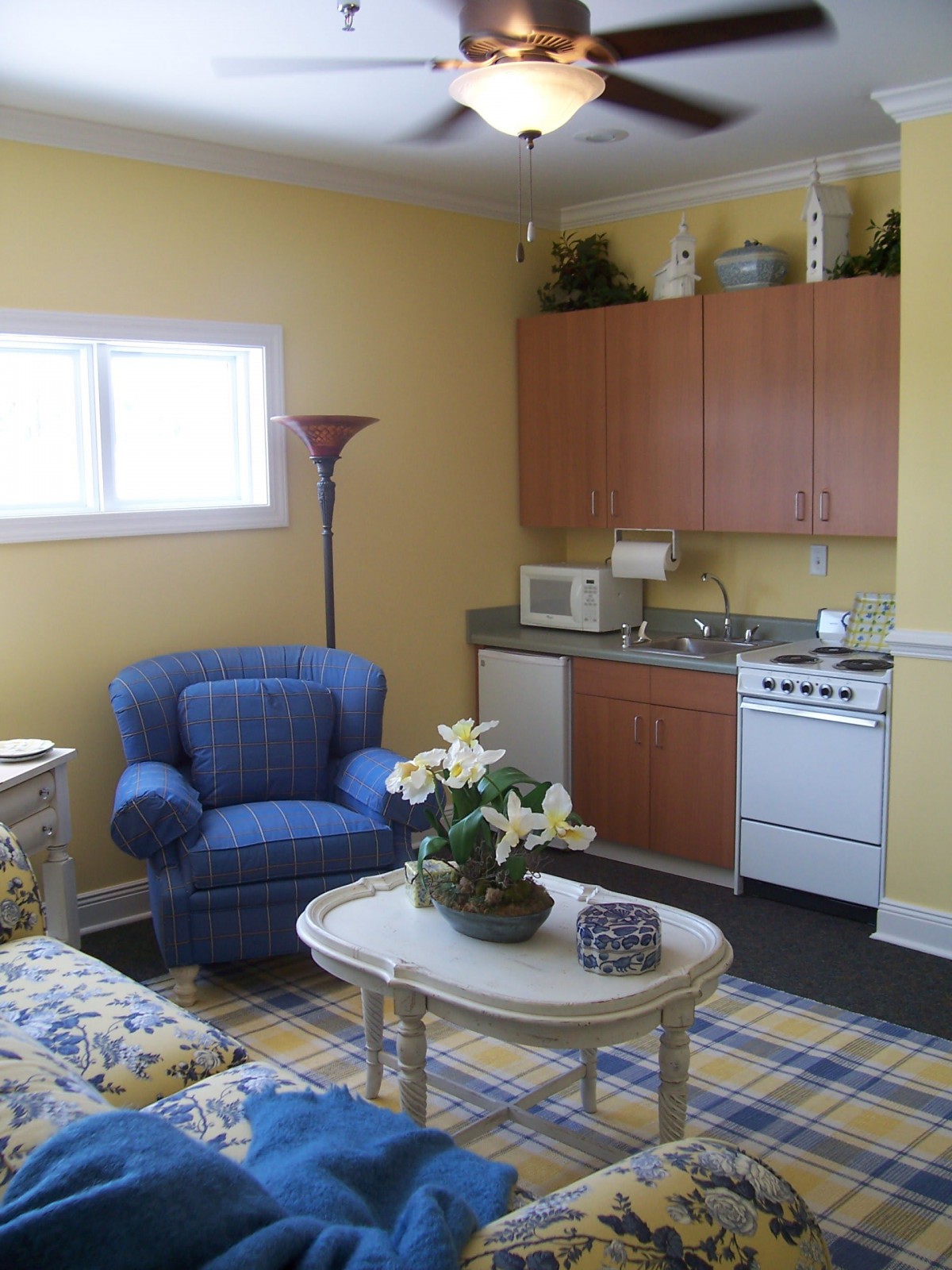 A cozy living area with a kitchenette, featuring an armchair, coffee table, and yellow walls.