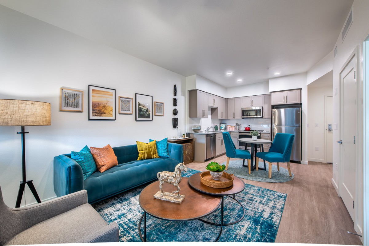 A modern open-concept living area with a blue sofa, colorful pillows, and a kitchen in the background.