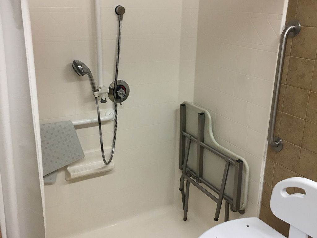 An accessible bathroom with a handheld shower head, grab bar, and foldable seat.