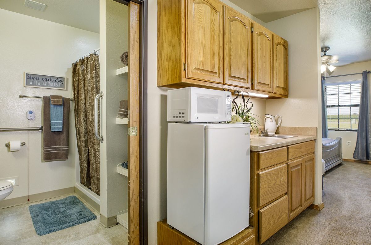 A cozy kitchen area with wooden cabinets, a microwave, and a fridge adjacent to a bathroom.