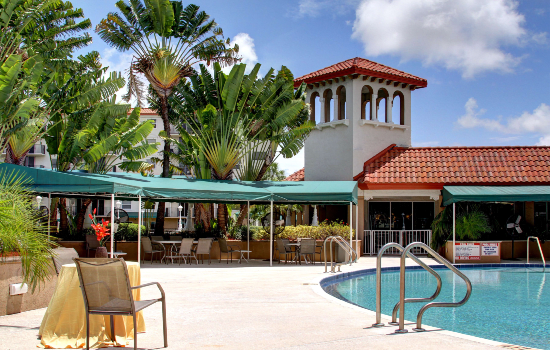 A tropical resort with a swimming pool and shaded seating area under clear blue skies.