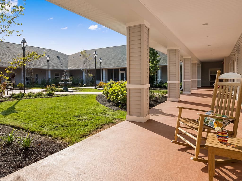 A sunny view of a landscaped outdoor patio with rocking chairs and a garden area, adjacent to a modern building.
