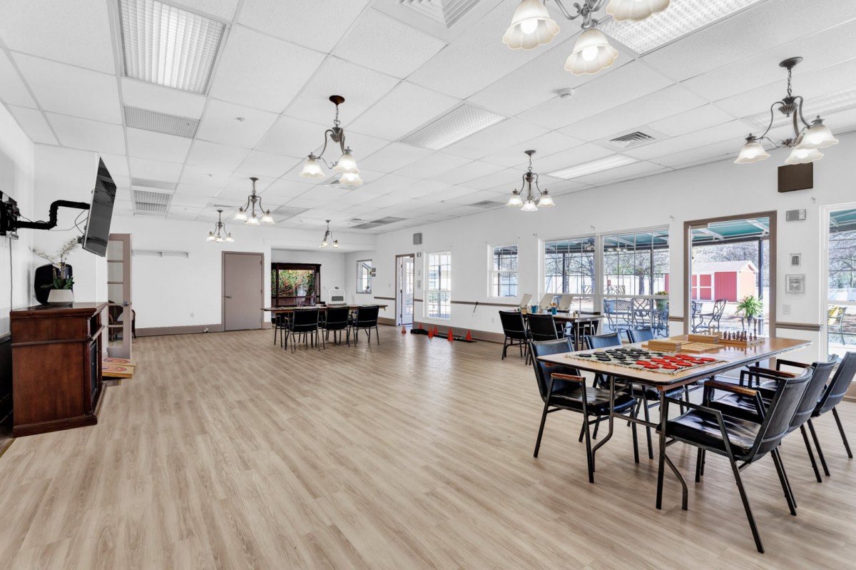 A spacious, well-lit room featuring tables and chairs, with large windows and modern lighting fixtures.