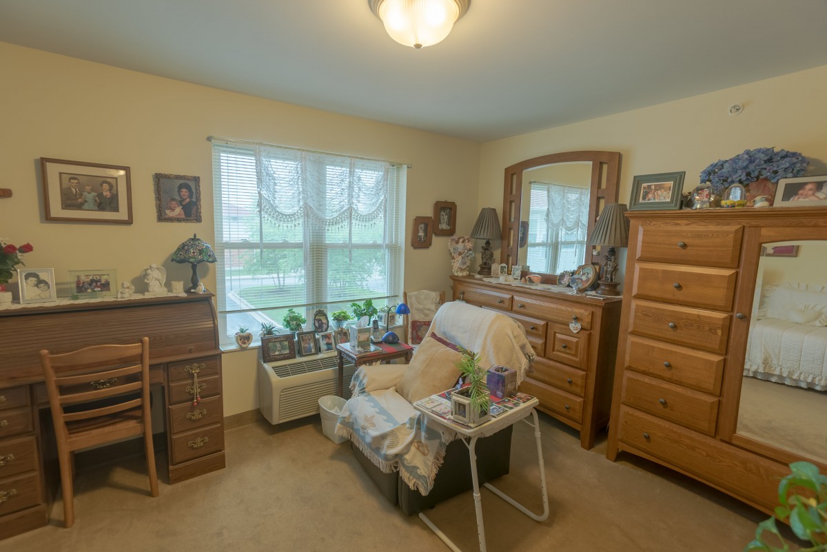 A cozy living room with an armchair and dresser by the window.