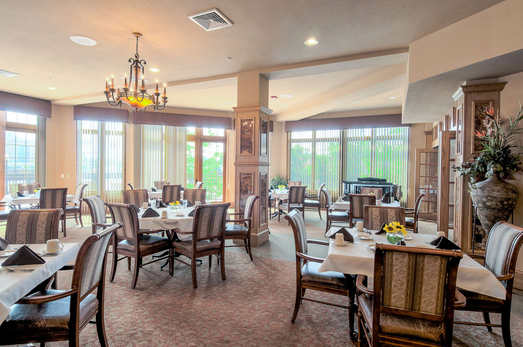 A cozy restaurant dining area with tables and chairs, featuring large windows and a chandelier.