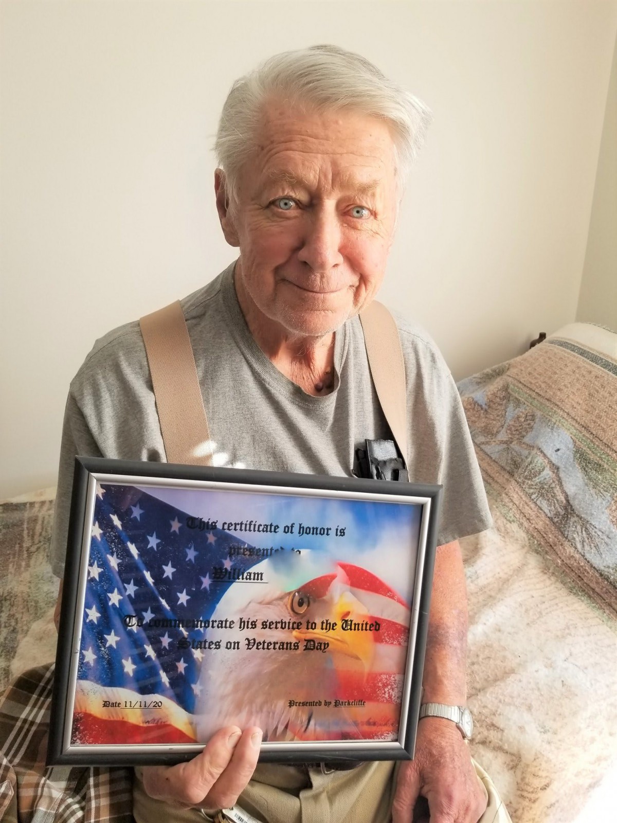 An elderly man proudly holds a framed award featuring an American flag.